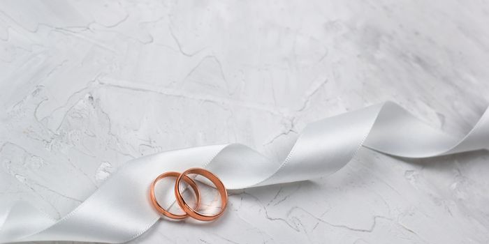 two golden rings and white satin ribbon wedding decor or wedding invitation background concept