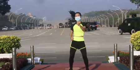 Exercise instructor does aerobics class while military coup takes place behind her